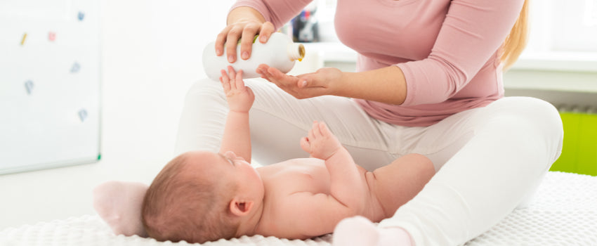Baby lying on a white blanket with a person in a pink shirt interacting.