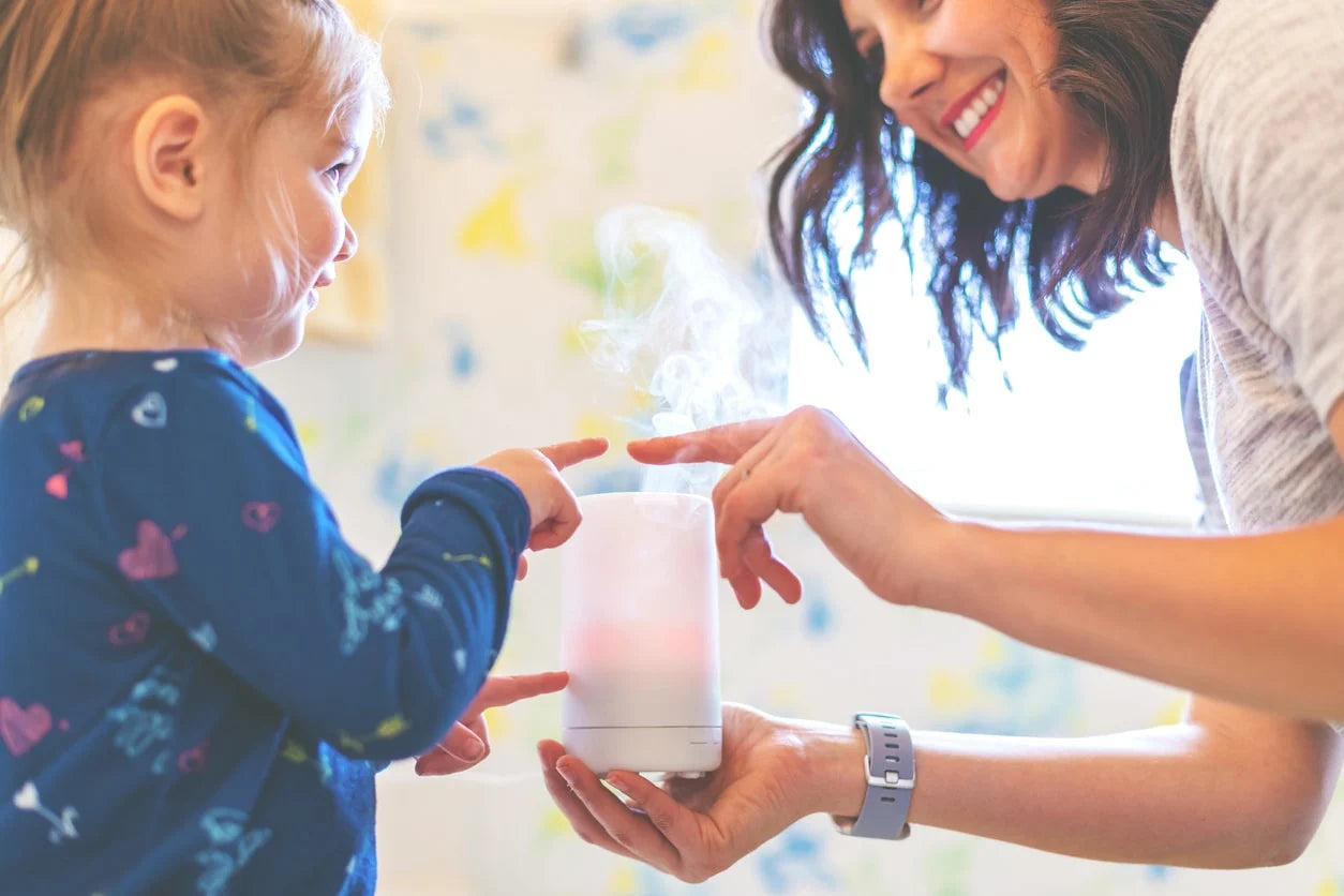 Woman and child interacting with a small device, possibly a toy or gadget, against a light background.