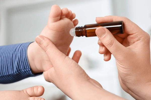 Person applying a small bottle of essential oil to a child's foot.